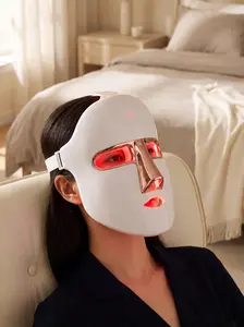 Woman relaxing in a bedroom while wearing the Lumoras LED face mask in red light mode